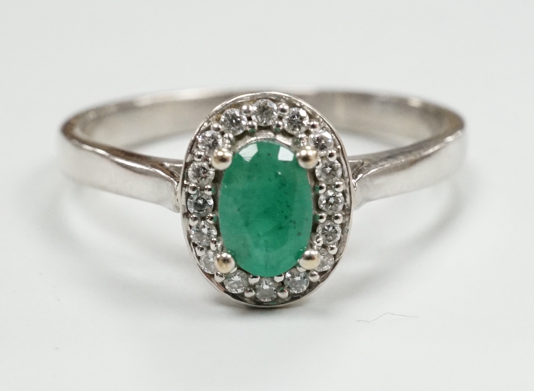 A modern 18ct white gold, emerald and diamond set oval cluster ring, size S, gross weight 3 grams.